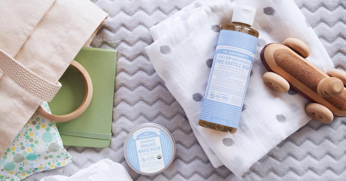 Dr. Bronner's baby soap and magic balm sit on bed alongside wooden baby toys, notebook, and more